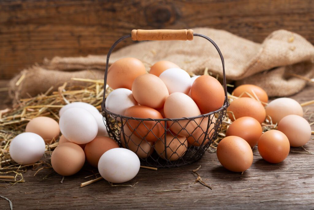 A wire basket full of fresh eggs on a wooden table.